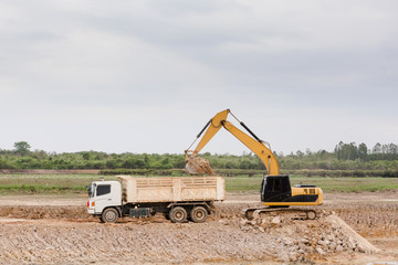 Fototapeta na wymiar Yellow excavator machine loading soil into a dump truck at construction site