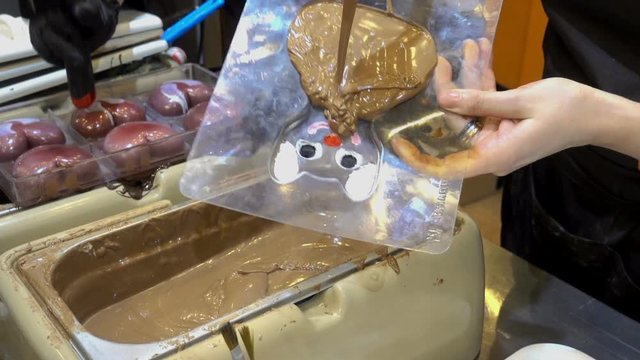 Chocolate making. Professional confectioners womans pours warm melted chocolate in plastic molds. HD video