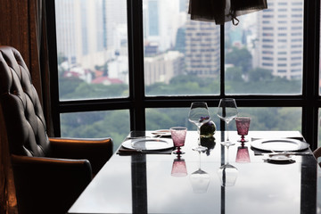 arranged table for 2 in a fine dining restaurant. modern cityscape visible through the window with reflections of sky and items on the table