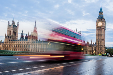 A fast moving double-decker bus crosses Westminster Bridge in London at sunrise.