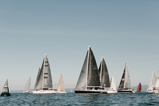 sailboats with dark sails lining up for yacht race to begin