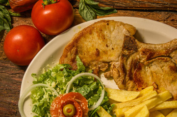 Delicious Lamp chop with french fries, tomatoes and lettuce served in a white plate over a wooden table background