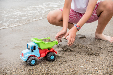 boy playing on the shore of the beach with a green, blue and red toy truck