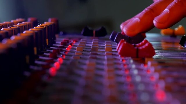 Hands close-up of sound control panel with knobs neon light at music recording session