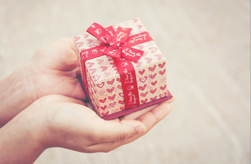 Close up female hand holding a small gift heart pattern. With red ribbon