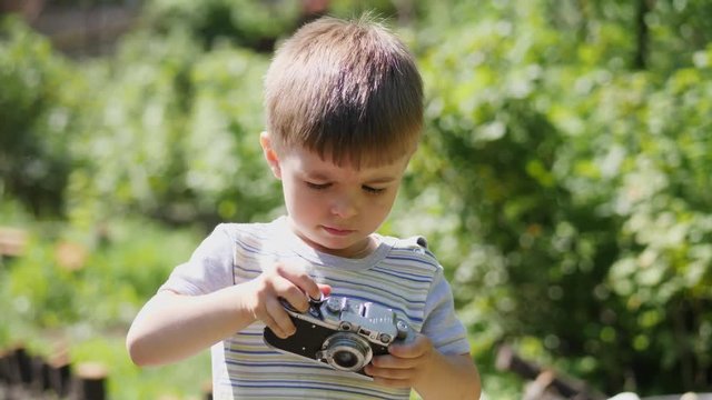 Portrait of a lovely little boy taking pictures outdoors on the vintage camera. Slow motion shot