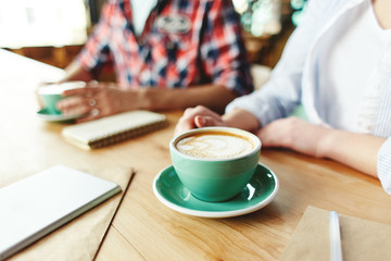 Crop shot of friends with notepad at desk having freshly made coffee in green cups.