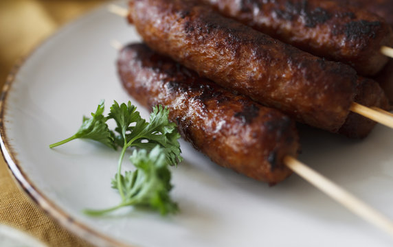 Cevapcici on wooden skewers with onions, parsley and ajvar