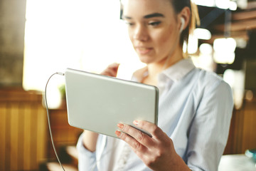 Close-up of touchpad in hands of young girl wearing headphones and surfing pad in leisure.