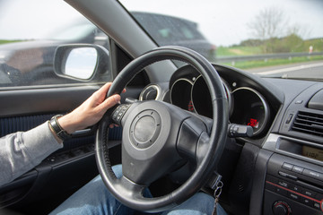 relaxed man holding steering wheels one hand during ride. fuzzy car in the window next to the driver
