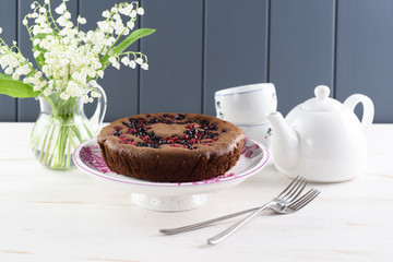 Healthy low calorie dessert. Tasty rustic cake with bird cherry flour, cowberries and black currants served with white teaware and lily of the valley bouquet on white background