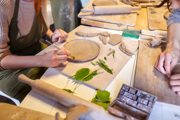 Earthenware. Ceramic products from raw clay. Stack, bowl, rolling pin lying on a wooden table. Art therapy lessons. Nerikomi technique. Girl draws vegetable patterns on the surface of a plate
