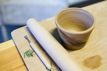 Earthenware. Ceramic products from raw clay. Mug, stack, rolling pin lying on a wooden table. Art therapy lessons. Nerikomi technique