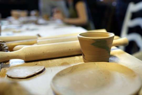 Earthenware. Ceramic products from raw clay. Mug, bowl, rolling pin lying on a wooden table. Art therapy lessons. Nerikomi technique