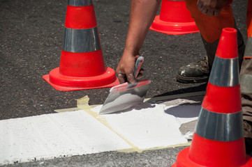 closeup of workers painting a white pedestrian crosswalk at a street with orange cones for safety