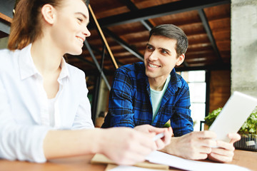 Obraz premium Content young woman and man sitting at table with notepad and talking happily sharing with ideas