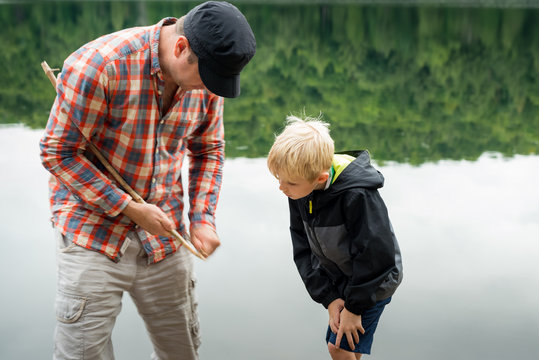 Father Showing Son How to Sharpen a Stick With a Knife While Camping