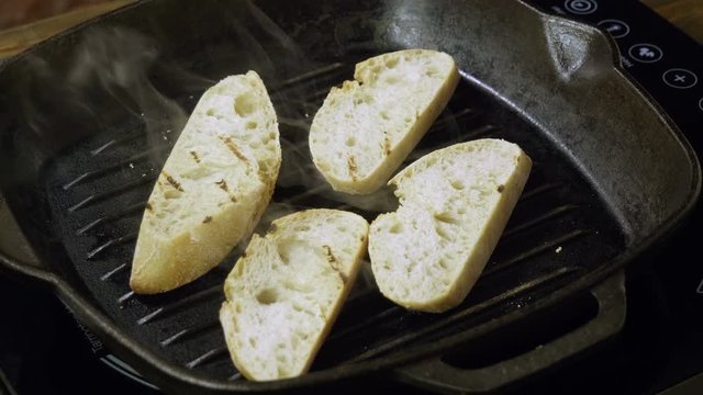Close-up shot of four slices of baguette are being fried in a grill pan for italian bruschetta. 4K