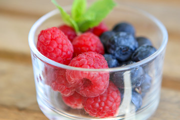 Raspberry and blueberry with green leaf in small glass bowl, close-up, macro