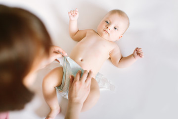 Female hands wearing pants for baby, a little kid lying on the bed nanny change diaper after bath,...