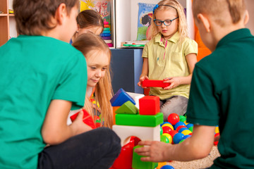 Fototapeta premium Children building blocks in kindergarten. Group kids playing toy on floor. Top view of interior preschool. Mat is big construction site building tower of cubes. Tournament of children's creativity.