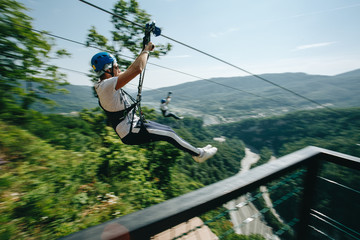 a brave man descends on a zip line high in the mountains above the forest