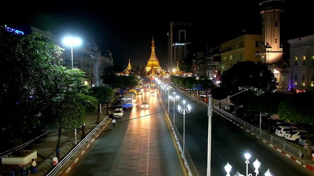 YANGON, MYANMAR - FEBRUARY 15, 2018: The evening view of Sule road with numerous public buses and the huge golden brightly illuminated stupa of Sule Paya on background, on February 15 in Yangon.