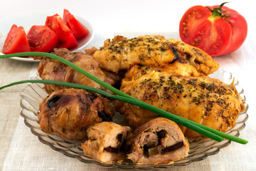 Cooked baked rolls from slices of meat with prunes, on top with green onions, in the background red tomatoes.