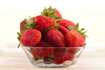 A large ripe strawberry with a glass plate on a linen tablecloth.