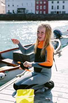 Female child in a wetsuit sitting on a jetty catching crabs.