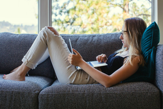 Profile Of A Teenage Girl Sitting On The Couch Looking At Her Laptop