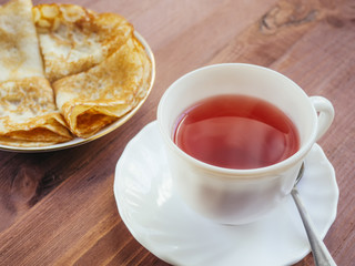 Cup with tea and a plate with pancakes on a wooden table