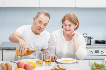 Obraz na płótnie Canvas an elderly man pours his wife juice for breakfast