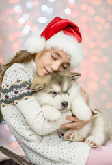 Fototapeta na wymiar little girl in red santa hat hugging puppy on a background of the Christmas tree