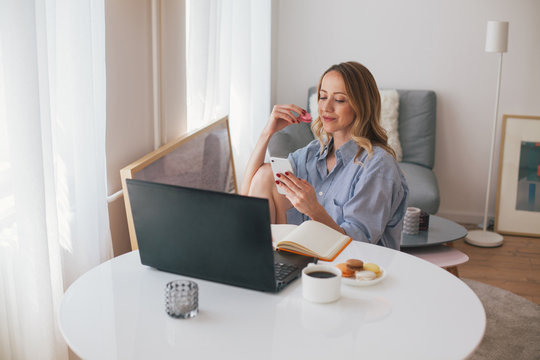Woman browsing on her mobile phone and eating macaroons