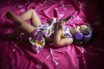 A kid lying down on bed and listening music with headphone