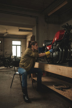 Young female working on restoration of old /vintage motorbikes in old rusty motorbike garage/workshop