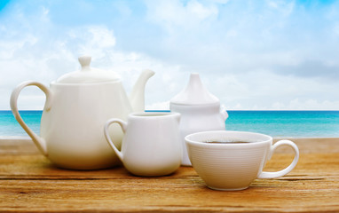 Tea coffee set on the wooden table at the Summer beach background. Sand and sea and sky
