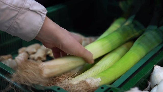A young woman chooses and buys a leek in a supermarket in the vegetable department.