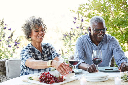 Mature African American couple drinking wine and eating lunch outdoors on the patio at home