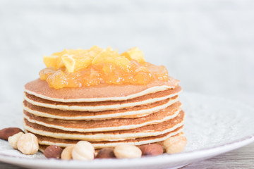 Stack of pancakes on a vintage plate with nuts and orange jam. Front view. Copy space