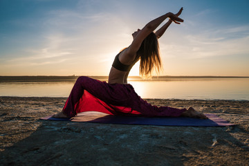 Fototapeta na wymiar Silhouette woman on the beach at sunset doing yoga asana. Morning natural stretch warm-up training