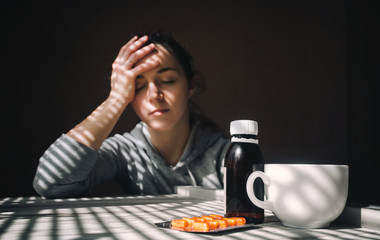 Headache. Morning. The girl holds her hand to her head. Tablets and a cup of water.