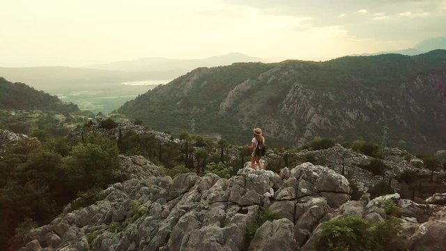 Aerial view of Young traveling woman wearing hat walks on high on the top of the mountain, evening with sunset. Montenegro
