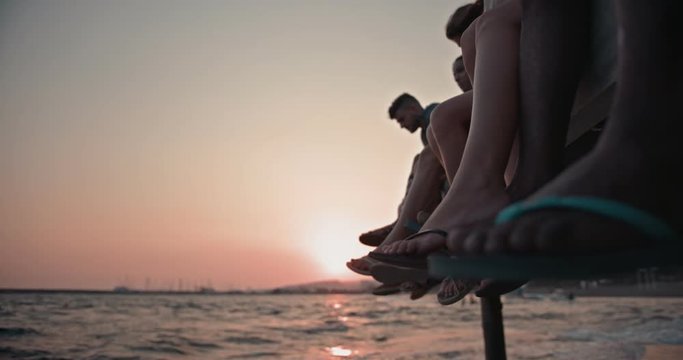 Multi-ethnic friends sitting on pier with their legs hanging down