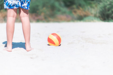 caucasian kid standing on the beach sand with ball next to him