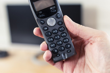 Cordless Telephone in Hand with Computer Monitor in Background