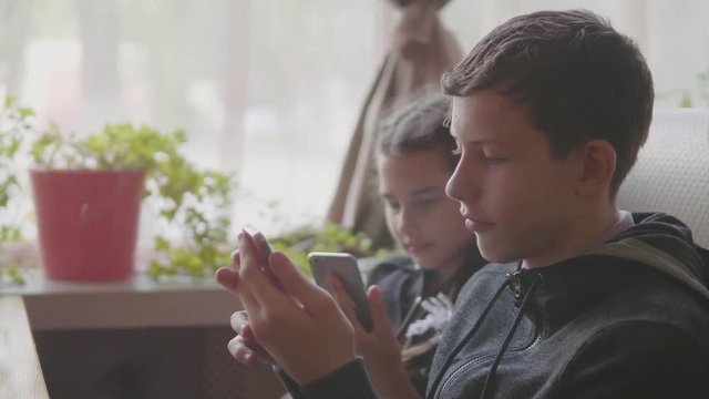 children are sitting in a cafe playing games in the smartphone slow motion video. boy and girl teens social media on smartphone. kids children and lifestyle smartphone concept