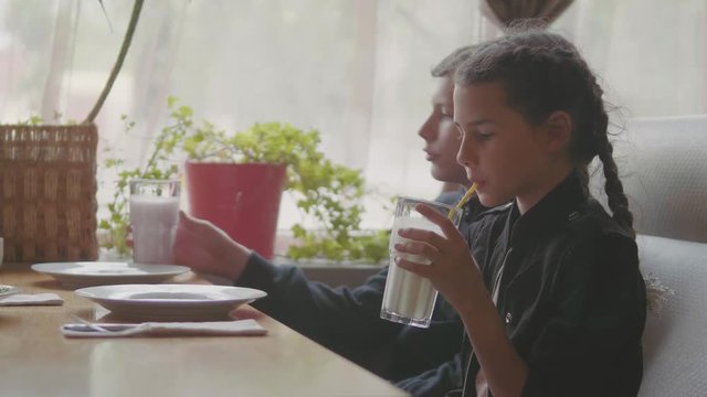 Two Cute kids drinking milkshakes or flavored drinks together indoors slow motion video cafe fast food. boy and girl teenagers drink milkshake at the cafe lifestyle concept