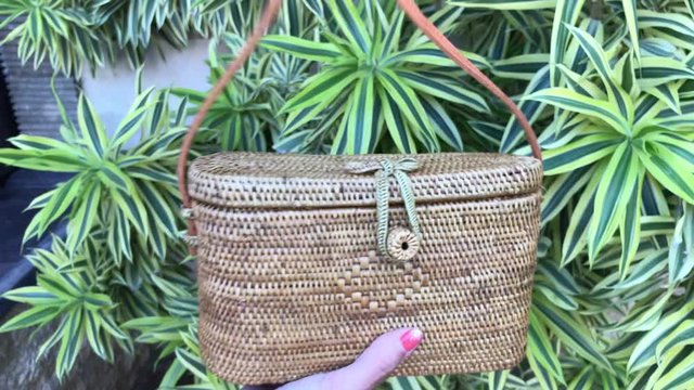 Closeup of woman hands with handmade stylish rattan handbag. Ata bag, eco bag. Rattan bag on a green nature background.